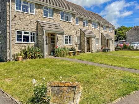Stone row houses with front doors, windows, grass lawn, and a stone sign reading Chestnut Court in West Lulworth