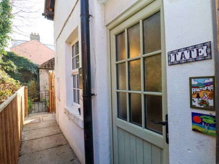 An exterior view of a house entrance with a door and window along a narrow pathway at Tate Cottage in Whitby