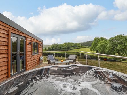 An outdoor deck with a hot tub chairs and a table overlooking green fields at The Cabin at Evelyns Retreat in Glyndyfrdwy
