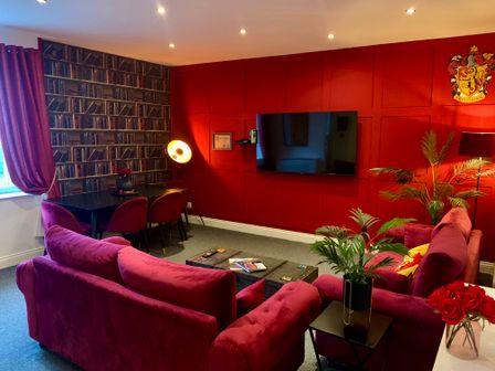 A living room with red sofas a wall mounted tv a table with chairs and a plant at The Wizard's Loft in Alnwick