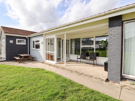 An outdoor patio area with chairs and a small table next to a lawn at Marsh Bungalow in Lowestoft