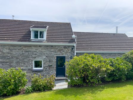 A stone cottage with dark roof tiles a dark door and windows surrounded by green bushes and grass at The Granary @ Canllefaes in Penparc near Cardigan