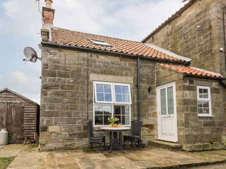 A stone cottage exterior with a tiled roof a small patio table with two chairs and a white door at Hawthorn Dale Cottage in Whitby