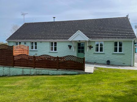 A single-story house with a green door and windows with white frames behind a wooden fence on a lawn at The Wheel @ Canllefaes Penparc near Cardigan