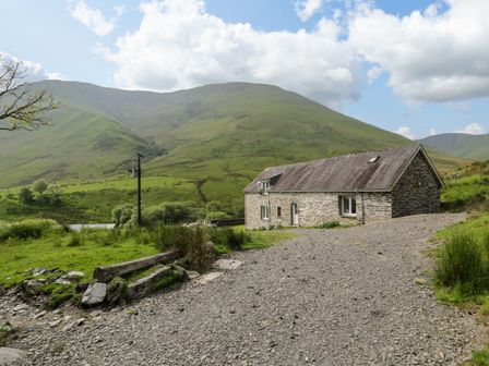 A stone cottage with gravel driveway in a green valley with hills in the background at Pennant Tigi Uchaf in Dinas Mawddwy