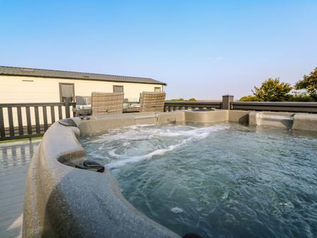 An outdoor hot tub with bubbling water next to a dining table and chairs on a deck at Chantry Lodge in Hendra Croft near Goonhavern