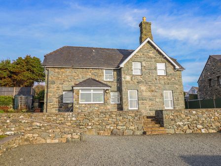 The exterior of a stone house with multiple windows a chimney and a stone wall with steps at Ty Cerrig in Dyffryn Ardudwy