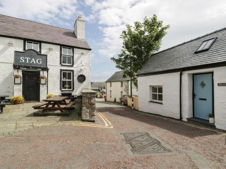 An outdoor area with a building labeled the stag and a bench beside a street with a white building at Llofft Penwaig The Herring Loft in Cemaes Bay
