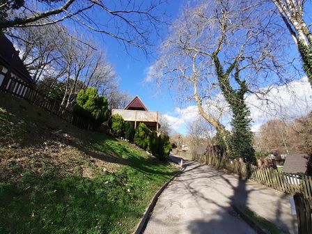 A paved road with wooden fences and A frame cottages along the side surrounded by trees with some greenery at Hillside in Gunnislake