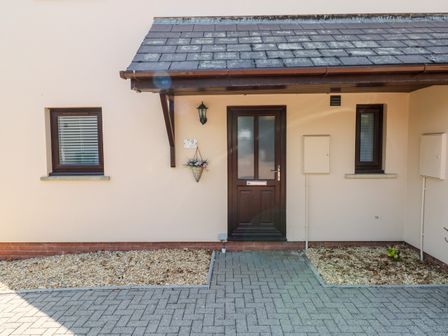 The front entrance of a house with a brown door and two small windows on either side at Clicketts Court in Tenby