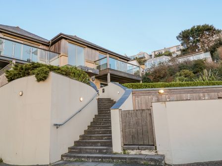 Outdoor stairs leading up to a building with large windows and glass balconies with tiled roofs and surrounding greenery at A Stone's Throw in Downderry