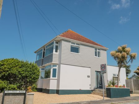 A two-story house with a pitched roof on Hillcrest Road with a 20 mph zone sign and plants in Wyke Regis