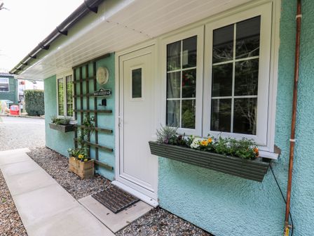 The exterior of a light blue cottage with a white door windows and flower boxes at Honeysuckle Cottage in Crossgates