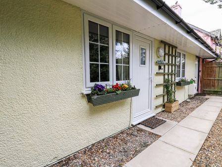 The exterior of a house with white door and windows with flower boxes on the wall at Primrose Cottage in Crossgates