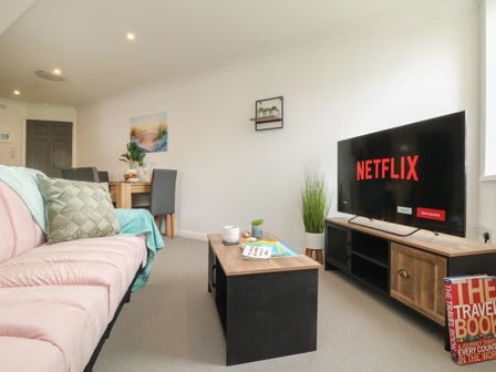 A living room with a pink sofa a wooden coffee table a television displaying Netflix and a dining table at Lighthouse Lofts - St Anthony in Camborne