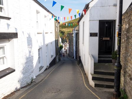A narrow street with white buildings decorated with colorful bunting flags and a door labeled wrens nest at The Moonbeach Cabin in Gorran Haven