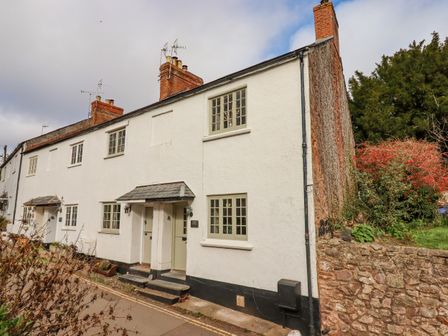 A row of white terraced houses with chimneys and small porches along a street at Bodkin Cottage in Dunster