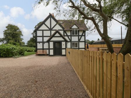 A black and white timber framed house with a wooden bench outside a wooden fence and trees at Lavender Cottage in Madresfield near Malvern