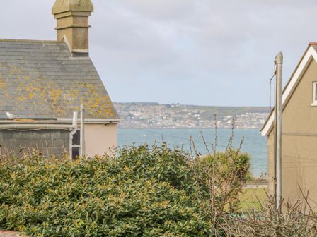 A view of rooftops bushes and a sea with a town in the background at Driftwood in Marazion