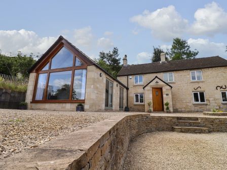 A stone house with a large window extension and a gravel driveway at The Nook in Jack's Green near Painswick