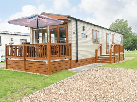 A mobile home with a wooden deck, outdoor table and umbrella at Audrey's Lodge Foxburrow Hang in Fritton