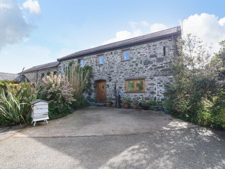 A stone house with wooden door and windows surrounded by plants and driveway at Ty Gwennol in Llanddona near Beaumaris