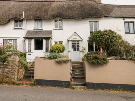 A thatched roof cottage with white walls and two front doors with steps and plants in front at Alexanders Cottage in Frogmore