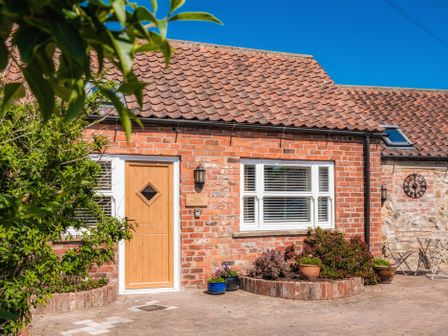 Exterior view of a brick house with a wooden door and windows with white blinds at The Old Milking Parlour in Skipsea