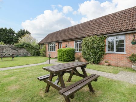 A garden area with wooden picnic tables in front of a brick building with windows at Owls Retreat in Brean