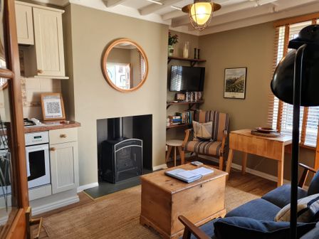 A living room with a fireplace wooden chest table an armchair wall-mounted TV and kitchen area at Pipit House in Whitby