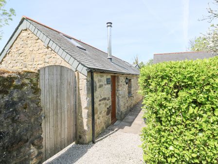 A stone building with a wooden door and gate next to a green hedge at Godolphin Barn in Ashton near Rosudgeon
