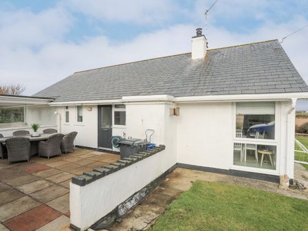 An exterior view of a single-story house with a tiled roof and a patio area with dining furniture at Didaro in Trearddur Bay