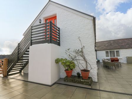 Exterior of a white building with black staircase and orange door with patio furniture and potted plants at Clementine Cottage in Manorbier