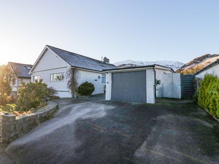 An exterior view of a single-story house with a garage driveway and garden at Hazelodge in Coniston