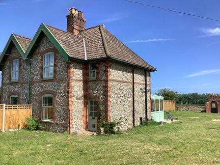 Stone and brick house with green trim and a tiled roof in a grassy yard with a small brick archway in the background at Owl Cottage in Southrepps