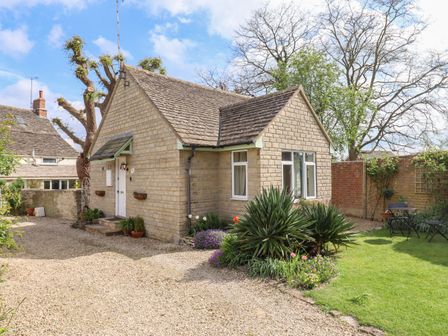 A stone cottage with a gravel driveway and garden with outdoor furniture at Straw Cottage in Cricklade