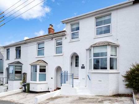 A white terraced house with bay windows a blue railing and a driveway at Blue Lobster Cottage in Port Isaac