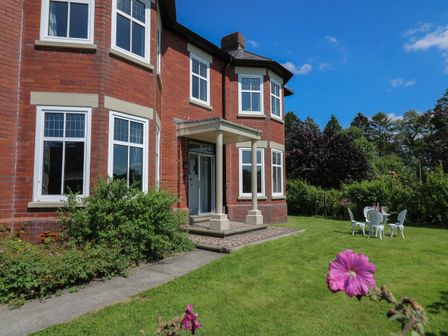 A brick house with white framed windows a small porch and a garden with green grass and white outdoor chairs and table at Tirallen in Llangadog