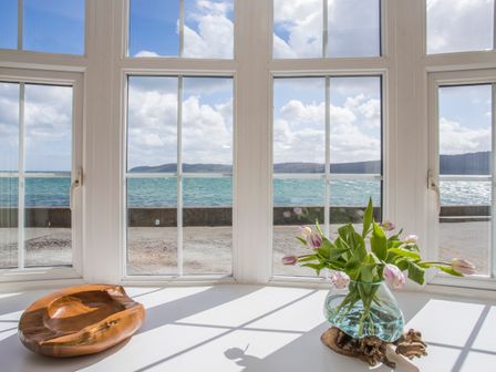 A window with a wooden bowl and a glass vase with flowers on the sill at 2 The Coach House in Red Wharf Bay