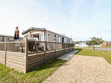 A mobile home with a fenced wooden deck and an outdoor umbrella on a grassy plot at Freddy's Lodge Foxburrow Hang in Fritton