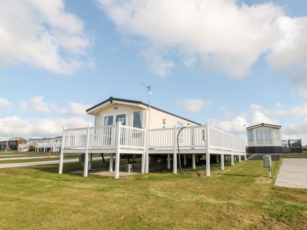 A mobile home with a white railing deck on a grassy plot at Moonlight Lodge in Bockenfield Country Holiday Park near West Thirston