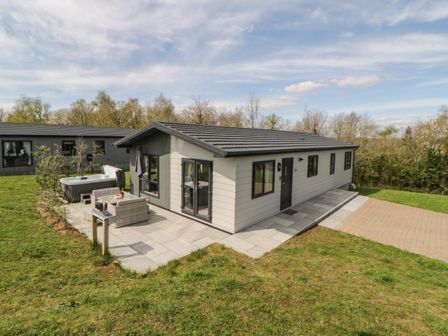 A single story house with an outdoor seating area and hot tub in a grassy yard at Meadow Lodge in Lifton
