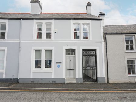 A street view of a two story white building with windows a door and a black iron gate at Cobblers Cottage in Beaumaris
