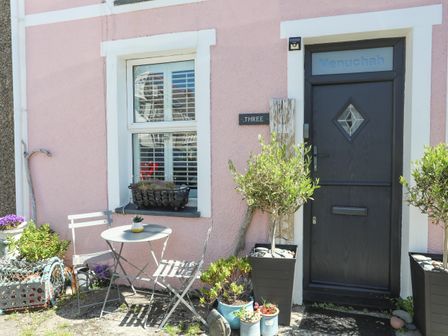 A small outdoor seating area with a table and two chairs next to a window and a dark door at Menuchah in Criccieth