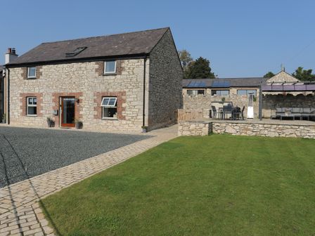 A stone house with a gravel driveway patio furniture and green lawn at The Stables in Penmon near Beaumaris