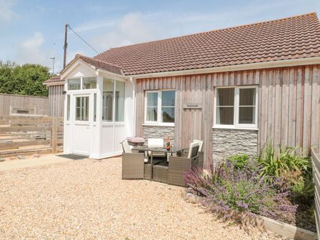 An outdoor seating area with a table and chairs in front of a wooden house with a tiled roof and a small garden at Garland in Nottington near Weymouth
