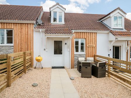 A patio area with a yellow barbecue grill a dining table with chairs and a wooden fence at Mellstock in Nottington near Weymouth