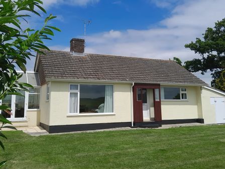 A single story house with a tiled roof a chimney and an antenna on a lawn at Broadstones in Bridport