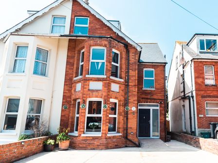 A brick and white semi detached house with bay windows and potted plants outside at Anchor House Weymouth