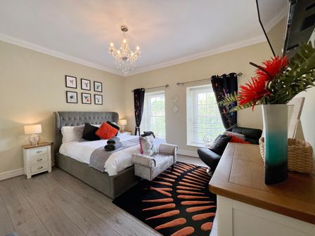 A bedroom with a bed pillows nightstands lamps carpet armchair dresser and windows at May Bell Cottage in Dersingham